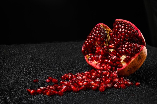 Photo the ripe grains pomegranate scatter from the half pomegranate on a dark textured background.