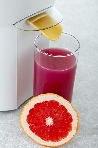 Ripe grapefruit slices in a juicer and a glass of fresh juice in the kitchen.