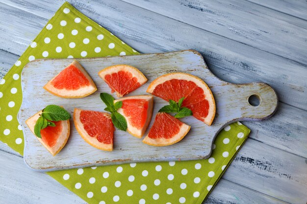 Ripe grapefruits on cutting board, on wooden table, on light background