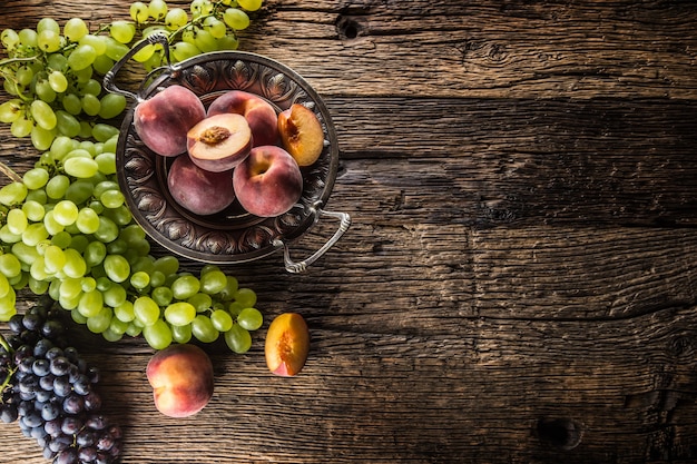 Фото Спелый виноград и персики в деревенском шаре и деревянном столе.