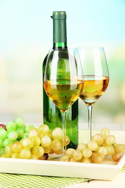 Ripe grapes bottle and glasses of wine on tray on bright background