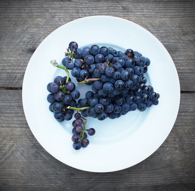 Ripe grapes on a white plate on wooden table background outdoors