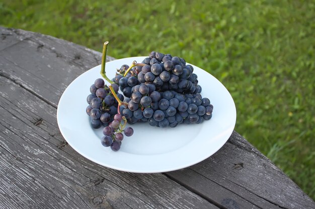 Photo ripe grapes on a white plate on wooden table background outdoors