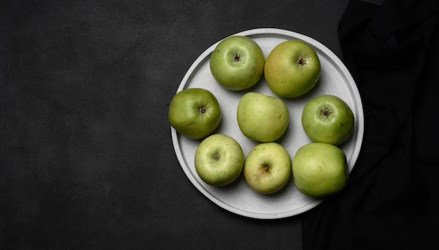 Ripe green apples on a gray plate top view on a black wooden table