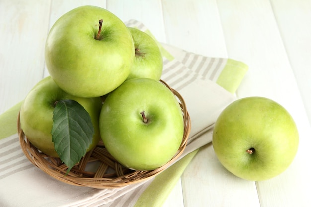 Ripe green apples with leaves in basket on wooden table