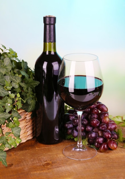 Ripe green and purple grapes in basket with wine on wooden table on bright background