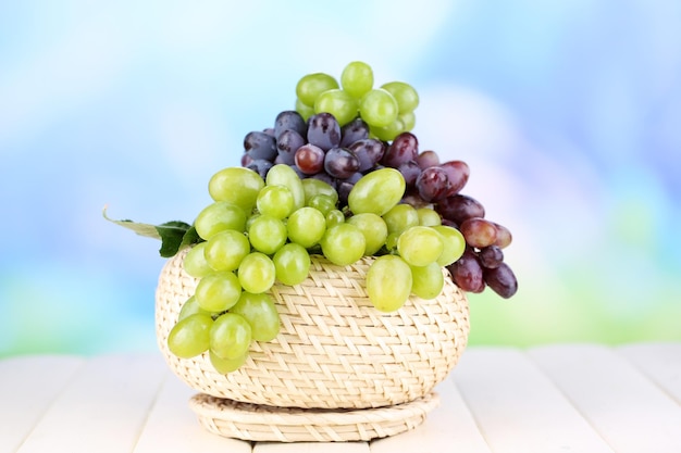 Ripe green and purple grapes in basket on wooden table on natural background
