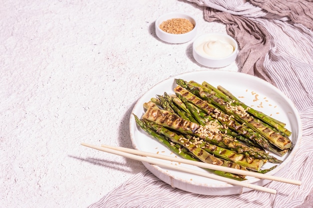 Photo ripe grilled asparagus. sauce, golden flax seeds, healthy and wholesome food concept. modern hard light, dark shadow. light putty background, copy space