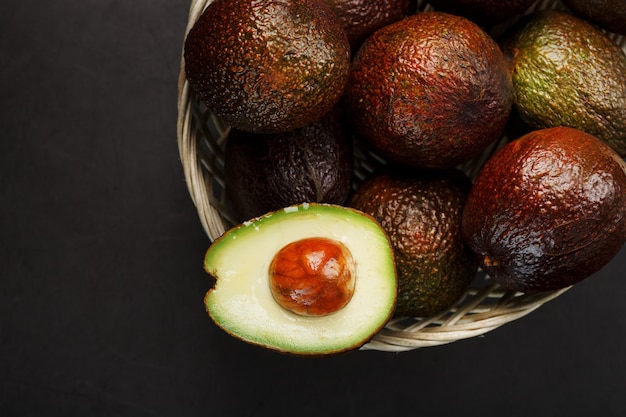 Avocado hass maturo e una fetta snocciolata in un cestino su una superficie testurizzata nera