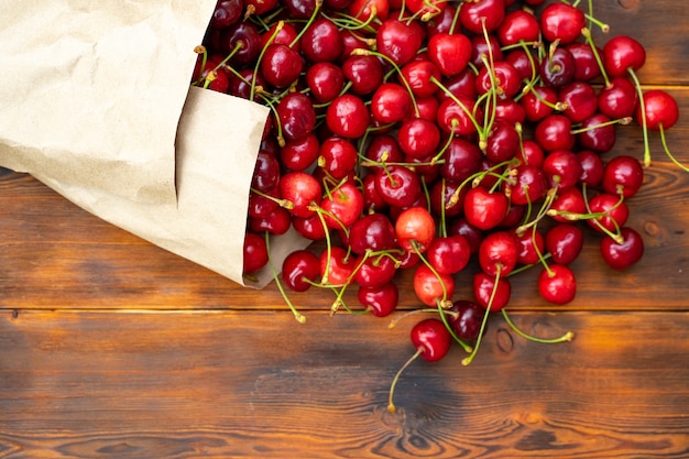 Ripe juicy cherries in a paper bag on a wooden table, selective focus