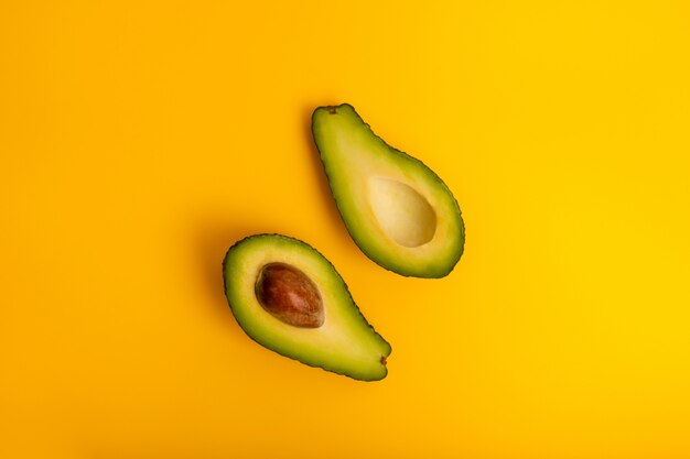 Ripe juicy halved  avocado on a yellow solid background with copy space. Vegan, vegetarian, raw organic food template. Eco detox style.