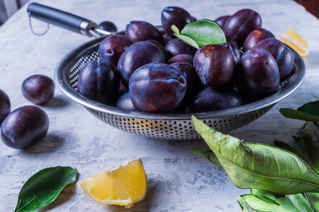 Ripe juicy plums on a colander, on old white wooden table.