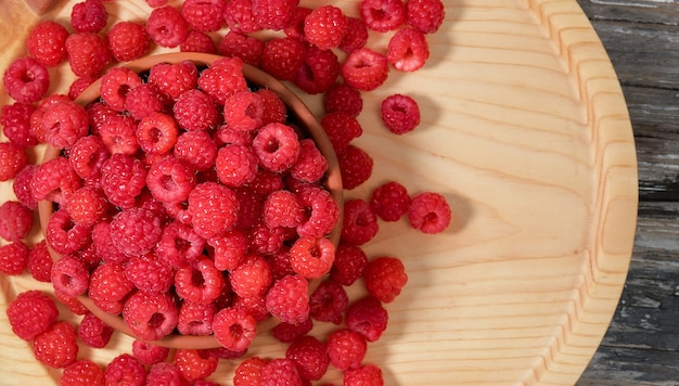 Ripe juicy raspberries in a bowl on a light wood background, flat lay with copy space. Ingredients in raspberry juice or desserts