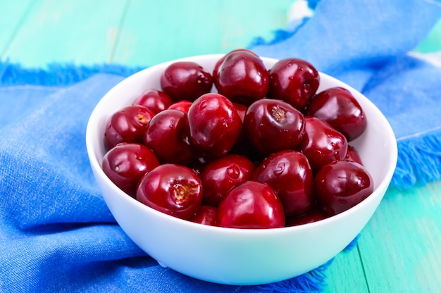 Ripe juicy red cherries in a ceramic bowl on a bright wooden background.