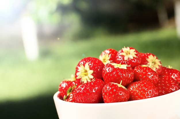 Ripe juicy strawberries in a bowl on a wooden background in the summer garden. Top view