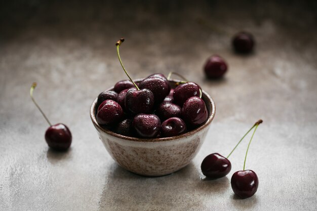 Ripe juicy sweet cherries with water drops in a ceramic bowl on dark background