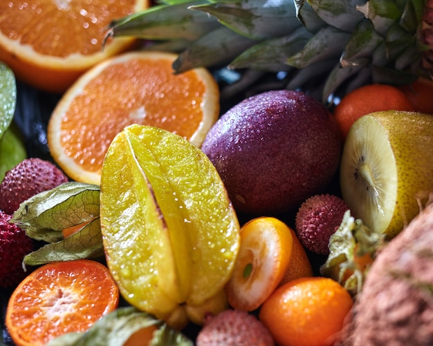 水滴の中の熟したジューシーな熱帯の夏の季節の果物-ゴレンシ、パイナップルの葉、キウイ、柑橘類、litci、パッションフルーツ。閉じる。健康的なダイエット食品の概念。