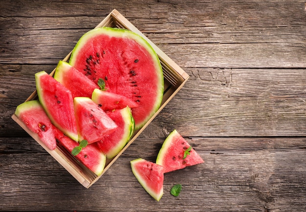 Photo ripe juicy watermelon pieces in box on wooden background. top view.
