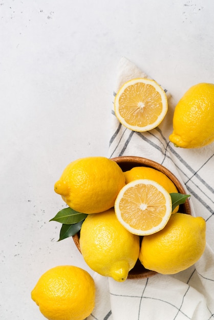 Ripe lemons in bowl with leaves on white. vertical top view