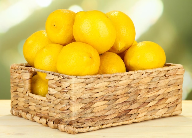 Ripe lemons in wicker basket on table on bright background