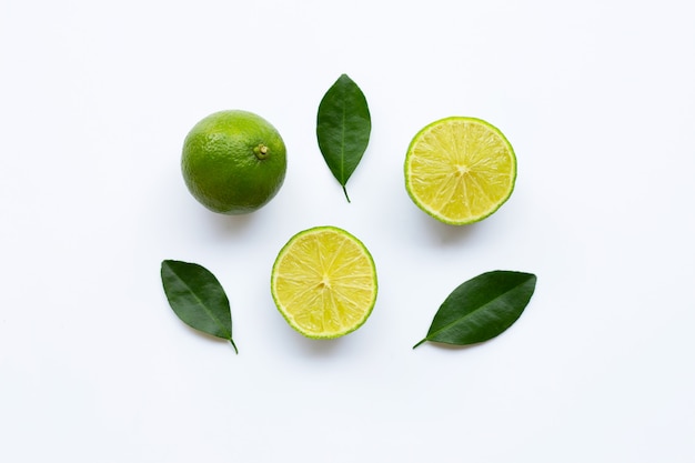 Ripe limes with green leaves on white.