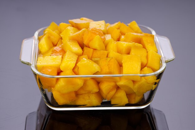 Ripe Mango cubes or cut piece arranged in a glass square container with black color background.