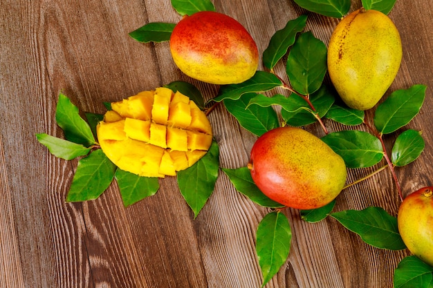 Ripe mango with leaves on wooden surface