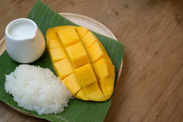 Ripe mango with sticky rice and coconut milk, thai dessert on banana leaf, wood texture