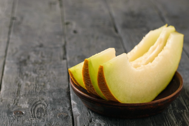 Ripe melon pieces on a clay bowl a wooden table.