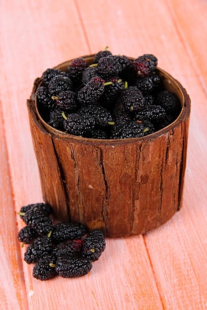 Ripe mulberries in bowl on wooden background