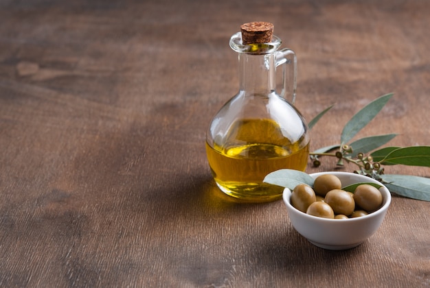 Olive naturali mature con olio in una bottiglia su un fondo di legno marrone