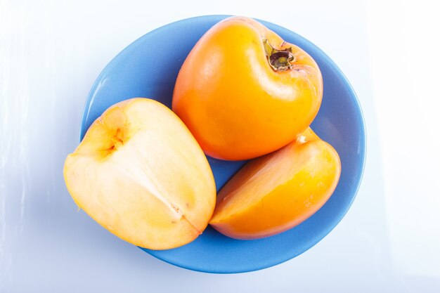 Ripe orange persimmon in a blue plate isolated on white background.