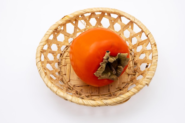 Ripe orange persimmon fruit in wicker straw basket. Isolated on white background.