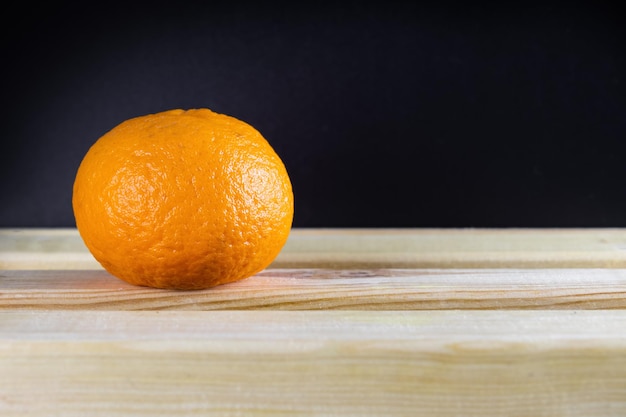 Спелый оранжевый мандарин на столе на темном фоне крупным планом