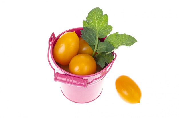 Ripe orange tomatoes in pink bucket on white background.