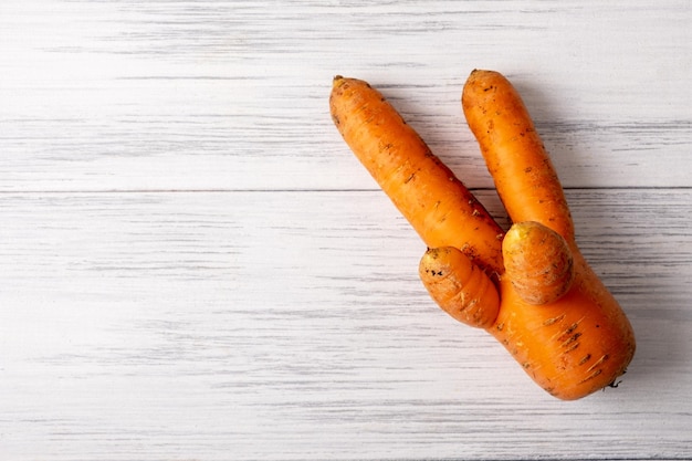 Ripe orange ugly carrots lie on a light wooden surface