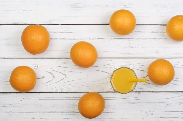 Photo ripe oranges and glass with juice on white wooden boards, top view