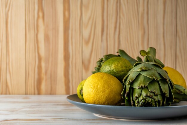 Спелые органические артишоки на белом деревянном столе с лимоном.