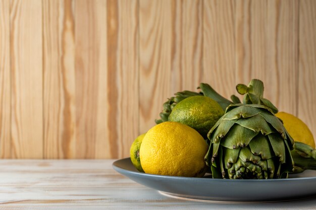 Ripe organic artichokes on a white wooden table with lemon.