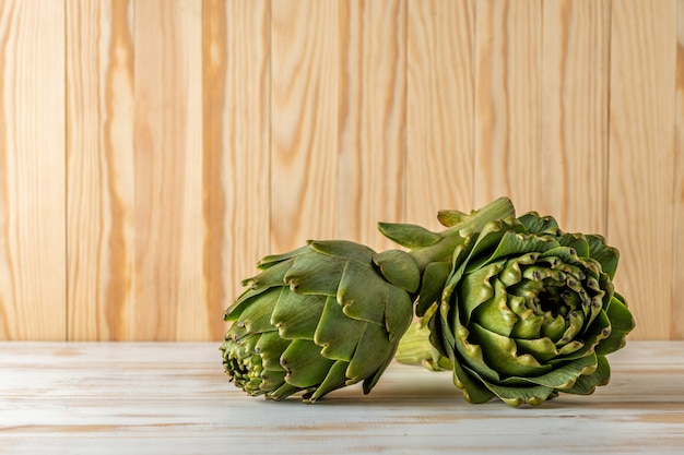 Ripe organic artichokes on a white wooden table.