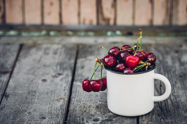 Ripe Organic Freshly Picked Sweet Cherries in Vintage Enamel Mug on Green Foliage Garden Nature surface