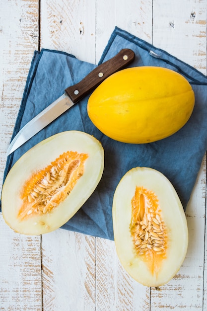 Ripe organic yellow melons, halved and whole on white plank wood garden table