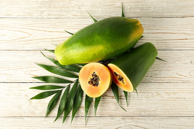 Ripe papaya with leaves on white wooden background