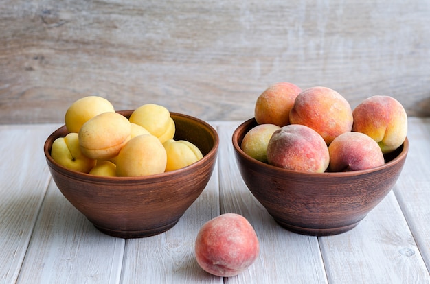 Ripe peaches and apricots in a clay dish on a light rustic table.