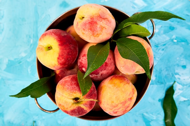 Ripe peaches in a bowl, basket on the blue table.