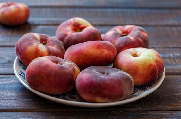 Ripe peaches in a clay dish on a dark rustic table.