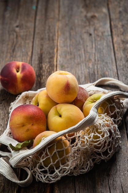 Ripe peaches in eco bag on wooden background