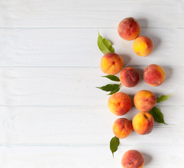 Ripe peaches on white wooden background top view