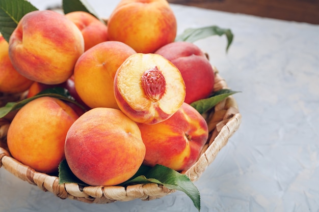 Ripe peaches in a wicker basket on a stone gray table with a juicy peach