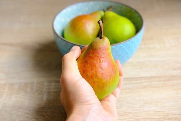 Ripe pear in female hand near blue plate on wooden background